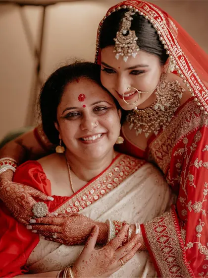 A heartwarming photo of the bride embracing her mother, both dressed in beautiful red and white sarees.