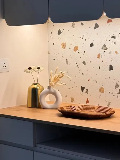 A detail shot of the crockery corner under warm lighting, highlighting the textures of the terrazzo, wood, and decorative vases.
