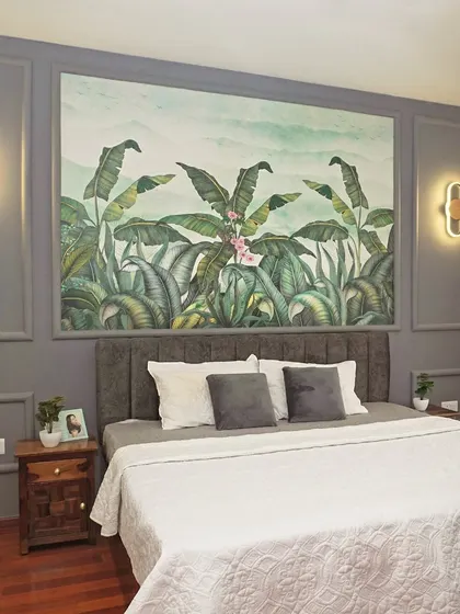 A beautiful master bedroom with a tropical-themed wallpaper accent wall behind a grey tufted headboard. The wall paneling and elegant sconce lights complete this serene and stylish look.