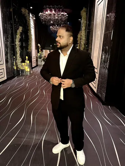 Posing in a stylish black suit at an elegant wedding reception. The ambiance of the venue, with its grand chandeliers and decor, sets the stage for a premium musical experience.