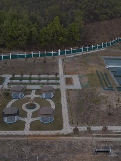An aerial view of the UNACCO School during construction, showing the layout of the main plaza, gazebos, and a large water body with a central pavilion.