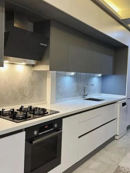 A full view of the sleek galley kitchen, showcasing the handle-less design and the seamless integration of the dishwasher. The reflective surfaces of the cabinets and countertop help to brighten the space.