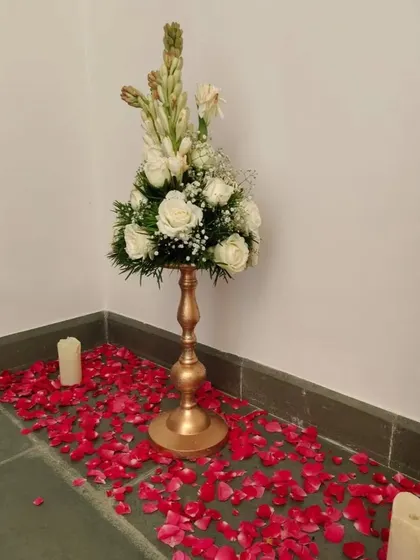 A single floral arrangement on a golden pedestal, with red rose petals scattered at the base. This is a simple way to add elegance to corners or entryways.