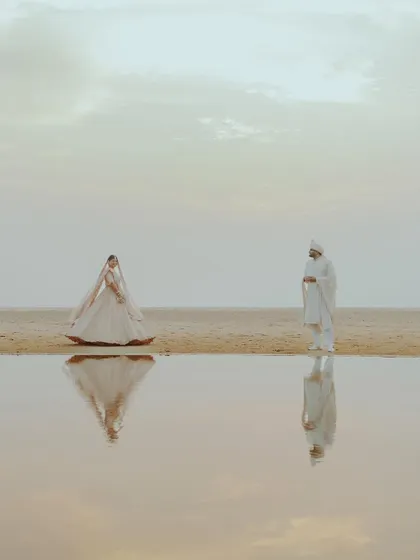 An artistic and serene portrait of a couple on the beach, their figures perfectly reflected in the calm water, showcasing our creative approach to couple photography.