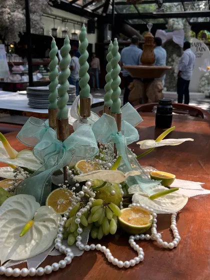 An elegant centerpiece featuring twisted mint-green candles, white anthuriums, fresh grapes, and pearls, tying the whole decor theme together.