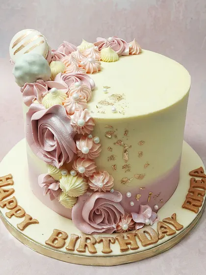 We design a cake that is as beautiful as a mother's love. This elegant creation features a cascade of dusty pink roses, delicate meringues, and shimmering gold leaf against a soft pink and white ombre, making it a perfect Mother's Day tribute.