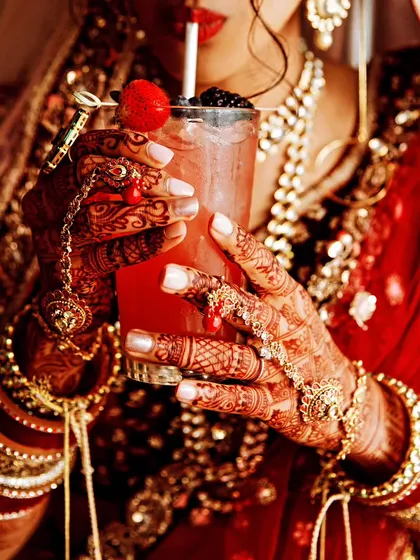 A lifestyle shot of a bride holding a refreshing drink, highlighting her intricate henna, bangles, and hand jewelry.
