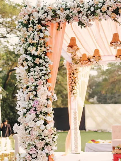 A close-up of a lush floral mandap pillar, showcasing the intricate arrangement of pastel roses and lilies that create a soft, romantic feel.