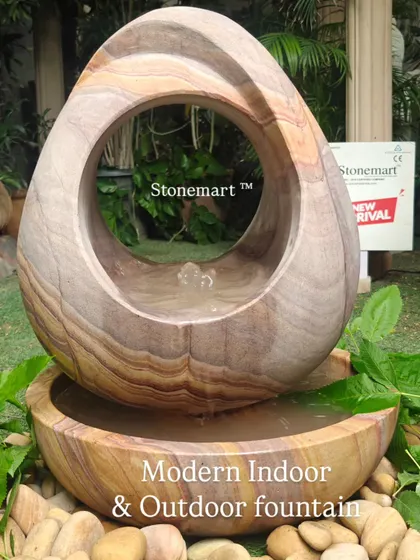 This view of the abstract Rainbow Sandstone fountain emphasizes its suitability for both indoor and outdoor settings, surrounded by natural elements.
