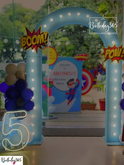 An exciting entrance for a 5th birthday superhero party, featuring "BOOM!" and "POW!" signs, a lighted arch, and a neon number "5".