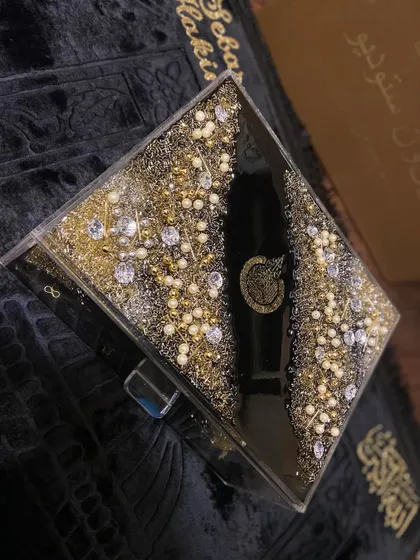 A close-up of the luxurious black and gold Quran box, showing the intricate crystal and pearl work.