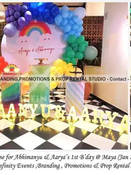 A vibrant rainbow theme for a twin first birthday at MAYA. The setup features a circular cloud backdrop with a rainbow balloon arch and marquee letters, creating a cheerful and colorful celebration for the twins.