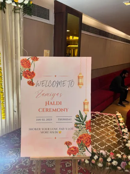A personalized welcome easel for 'Zamiya's Haldi Ceremony'. The floral design on the sign matches the overall theme of the event.