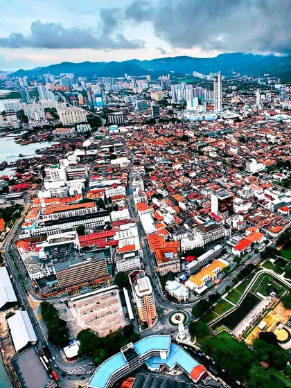 A wide aerial photograph of George Town, Penang, a UNESCO World Heritage Site. This shot captures the beautiful coastline and the dense, historic urban fabric of the city, taken during a project with AirAsia.