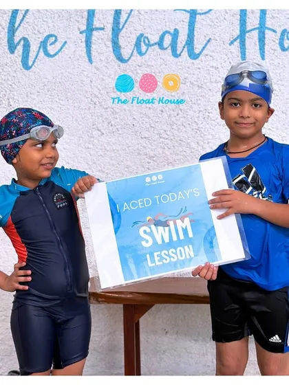 Two swim buddies proudly show off their 'I Aced Today's Swim Lesson' sign. Learning is always more fun with a friend by your side.