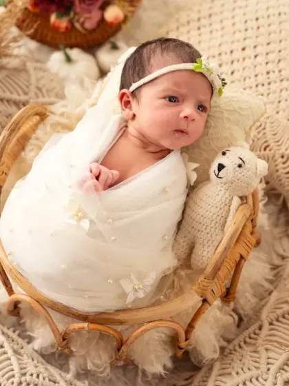 A curious baby girl looks to the side from her white swaddle and basket.