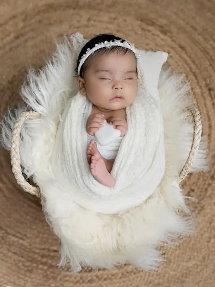 A simpler version of the heart-shaped basket setup, with the baby swaddled in a cozy white wrap. This minimalist approach keeps the focus entirely on the newborn.