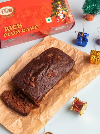 A close-up of our traditional Rich Plum Cake, sliced to show its moist, fruit-laden texture. This classic Christmas cake is a staple for any holiday gathering and comes in a festive red box.