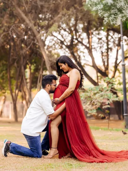 An intimate moment captured in a park setting. The partner kneels to embrace the baby bump, surrounded by the warm glow of the sun, creating a deeply romantic pregnancy photo.