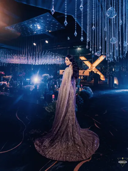 A breathtaking wide shot of the bride in a glamorous gown, standing in a lavishly decorated reception hall with a celestial theme.