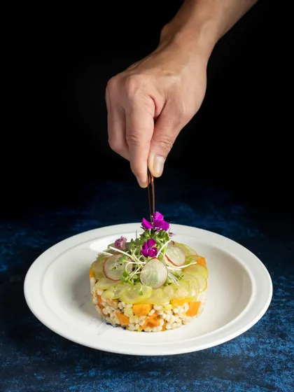A chef's hand carefully placing a garnish on a beautifully plated barley salad, highlighting the precision of gourmet cooking.