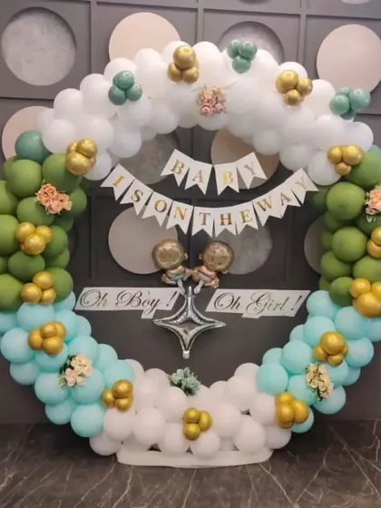 An elegant "Baby is on the way" baby shower decoration. A full ring of white, green, and blue balloons creates a beautiful frame for the announcement banner.