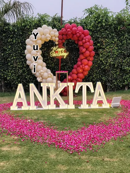 For a truly grand gesture, I can create large-scale outdoor decorations. This birthday surprise in a garden includes a heart-shaped balloon arch, a large heart on the lawn made from rose petals, and giant light-up marquee letters spelling out a name.