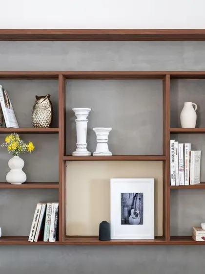 A close-up of the custom curio unit, showing the beautiful arrangement of books and decorative objects. The dark wood and concrete-finish background create a modern, moody aesthetic.