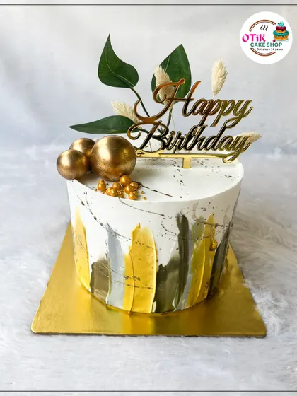 A modern and artistic birthday cake with a brushed watercolor effect in shades of green, yellow, and grey. Gold spheres and a leafy topper complete this stylish look.