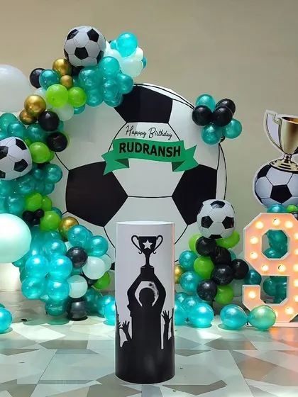A dynamic football theme for a 9th birthday. The decoration features a large football-shaped backdrop, a balloon garland in team colors, a trophy cutout, and a light-up number '9'.