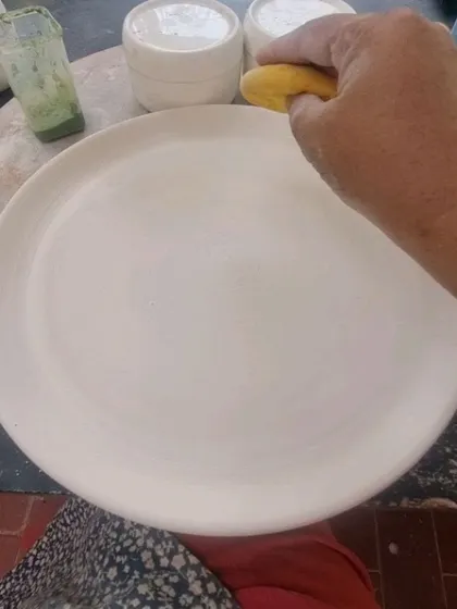 Smoothing the surface of a freshly thrown plate with a sponge. This is an essential step to prepare the clay for decoration.