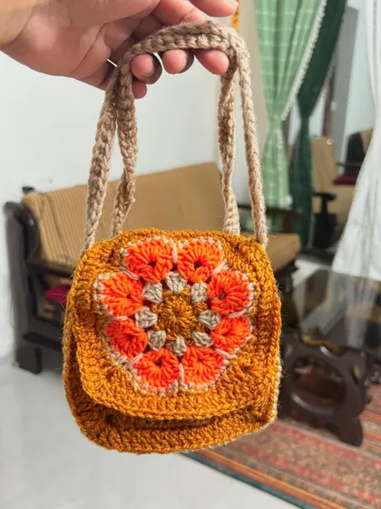 A handheld view of the small granny square sling bag, showing its compact size and detailed craftsmanship.