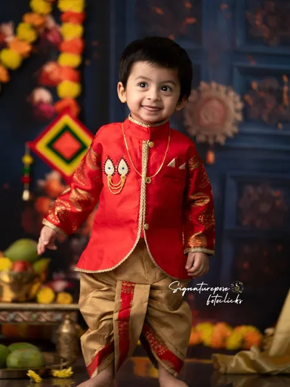 A handsome little boy dressed in a traditional sherwani and dhoti for a festive shoot. His happy expression and the vibrant, celebratory background make for a perfect portrait.