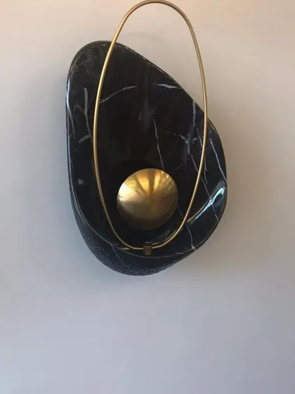 A detailed view of the 'Bird Nest' wall lamp. This piece showcases the beautiful contrast between the organic, polished black marble and the delicate, ring-shaped brass element that encircles the light source.