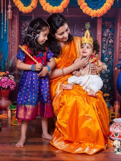 A heartwarming family portrait with a Krishna theme. Mom and big sister look on lovingly as the youngest is dressed as little Krishna, creating a beautiful memory for the whole family.