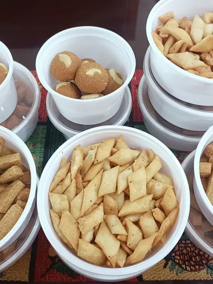 Laddus and namkeen are packed in tubs in our festive selection, with several wheat-snack shapes visible together.