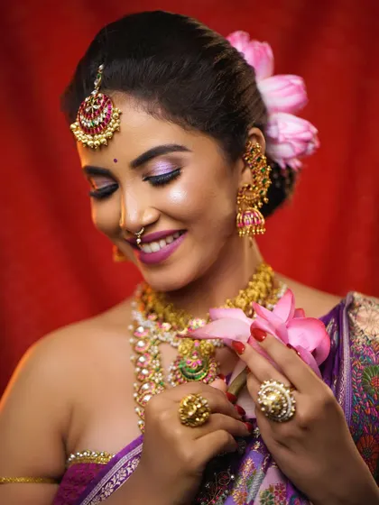 A gentle and serene portrait. The bride holds a lotus, tying into the soft pink and purple tones of her makeup and saree.