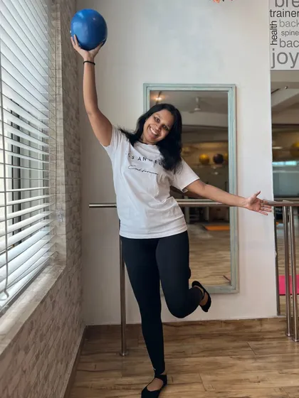 A member celebrates her strength and joy in movement, holding a Pilates ball with a triumphant smile.