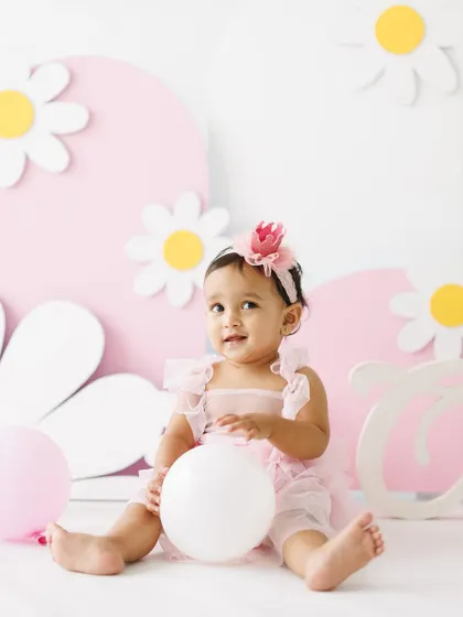 All smiles amidst the celebration. This little girl, surrounded by balloons and her birthday setup, looks so happy and content during her first birthday party photoshoot.