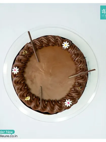 A top-down view of the Chocolate Truffle cake, showing the simple yet elegant arrangement of chocolate sticks and flowers on its smooth surface.