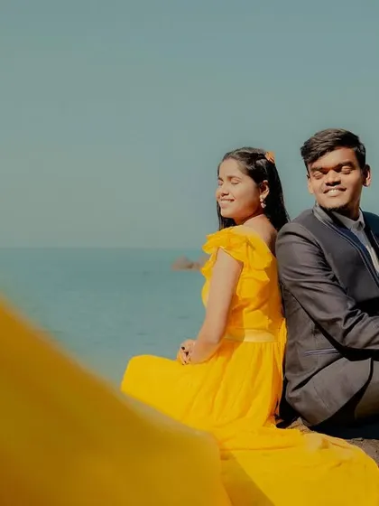 A playful and happy moment by the sea. The bright yellow trail of her gown is out of focus in the foreground, adding a creative and colorful element to this couple's photo.