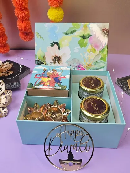 A simple and elegant Diwali gift box. This set includes two jars for dry fruits or sweets, a box of gourmet chocolates, and decorative diyas, presented in a lovely floral-printed box.