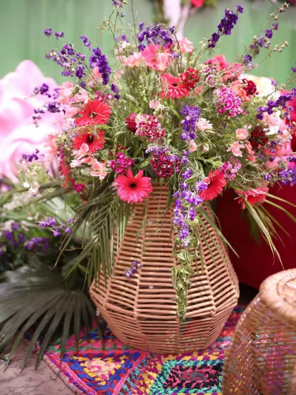 A vibrant bouquet of mixed flowers in a wicker vase. This arrangement combines pink gerberas, purple statice, and other colorful blooms, perfectly complementing a multi-hued mehndi theme.