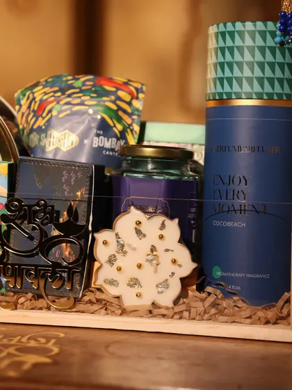A close-up of the details inside my blue-themed Diwali hamper, showing a 'Shri' cutout, a lotus-shaped candle, and a reed diffuser.