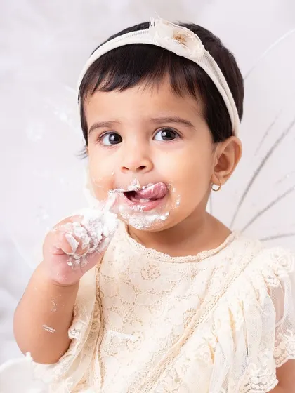 Just a little taste! This macro shot focuses on her cute face and messy fingers, highlighting the sensory experience of a first birthday cake smash.