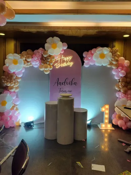A closer view of Aadrika's first birthday stage, highlighting the daisy-shaped balloon accents and the 'Happy Birthday' neon sign.