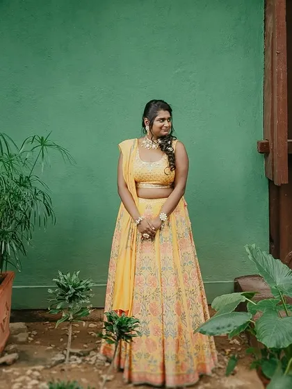 A bride in a yellow lehenga, laughing joyfully, a perfect candid moment captured in our gardens.