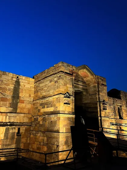 The illuminated ruins of the Quwwat-ul-Islam Mosque complex at the Qutub Minar site at dusk.