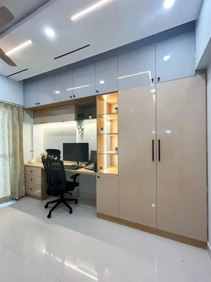 This minimalist study haven combines a wardrobe with a built-in desk. The glossy beige and grey cabinets provide ample storage, while the backlit panel illuminates the workspace.