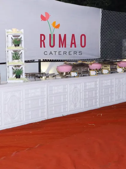 A clean and professional buffet setup featuring our "Rumao Caterers" branding. The white counters and pink chafing dishes can be customized to match your event's color scheme.